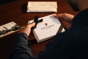 premium corporate gifting Hands holding a Pergamon London gift box on a wooden table, creating an elegant unboxing theme.
