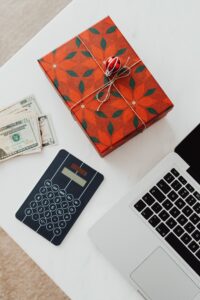 premium corporate gifting A beautifully wrapped gift box, cash, calculator, and laptop on a white table, symbolizing holiday expenses.